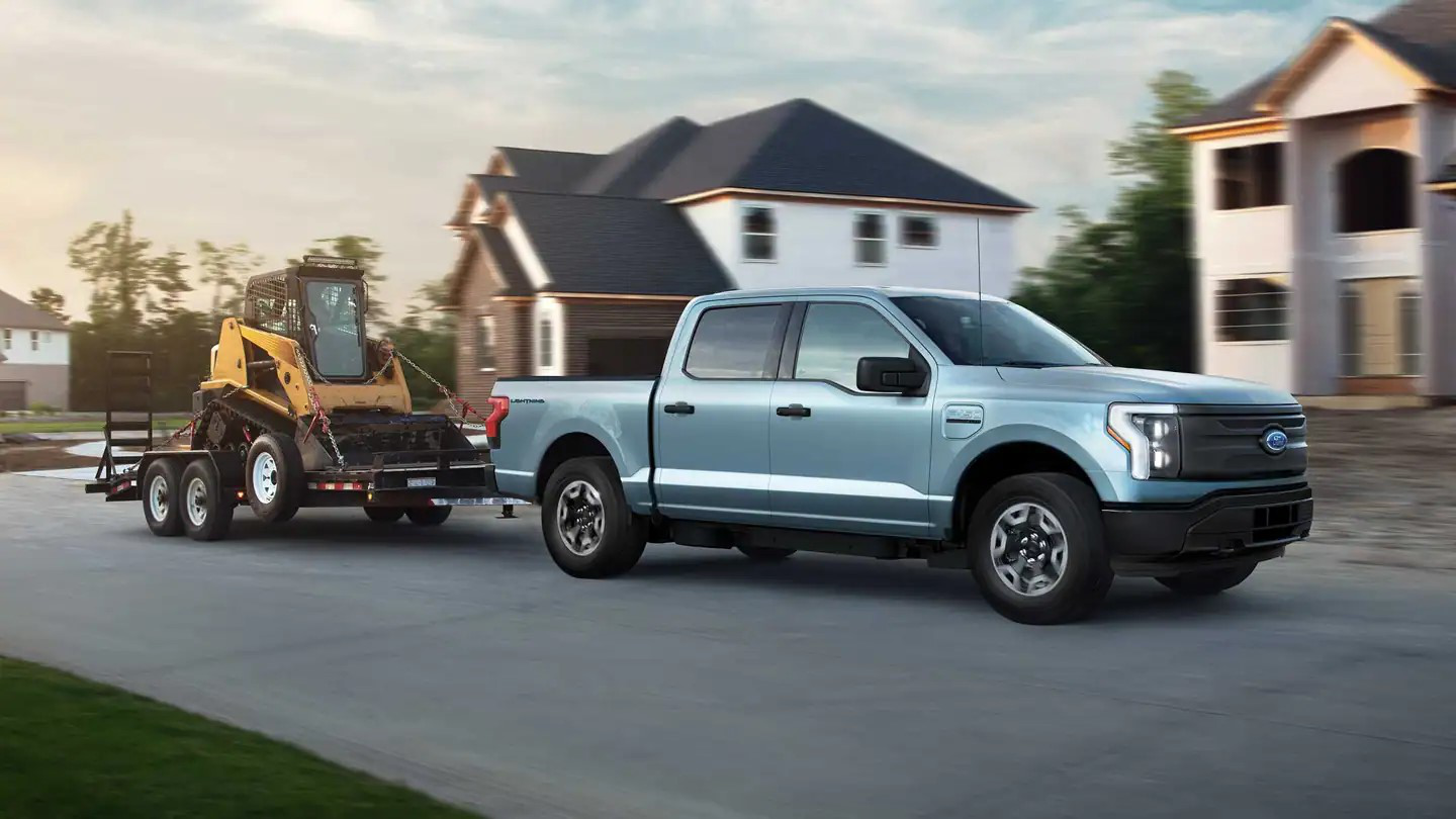 Ford F-150 Lightning Pro towing a trailer with construction equipment through a neighborhood in North Carolina.